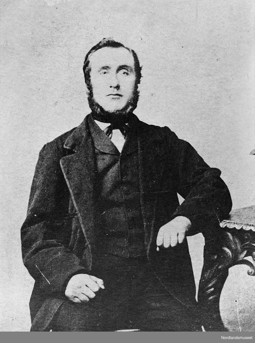 Portrett av mann med kinnskjegg, sitter ved et bord.