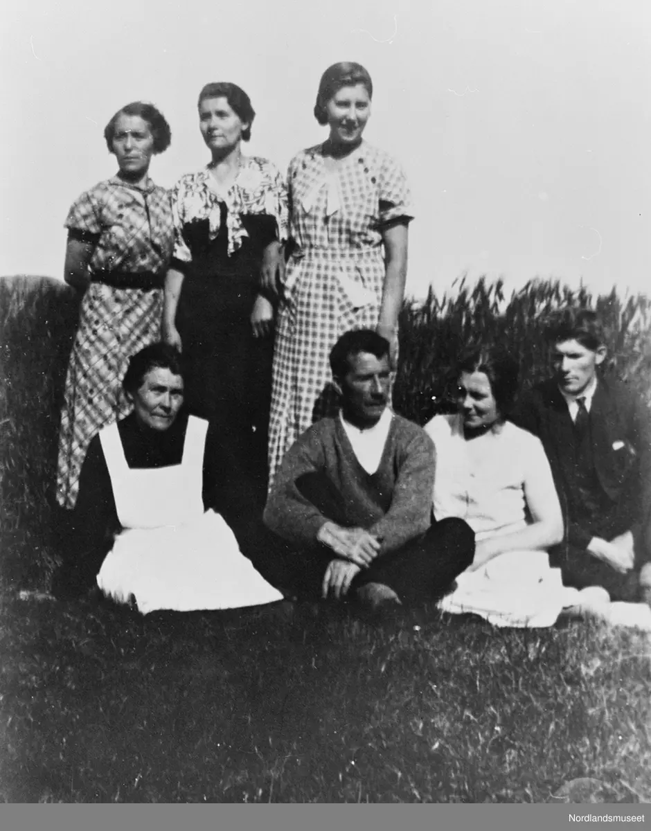 Tre damer som står bak to damer og to menn som sitter på marka.