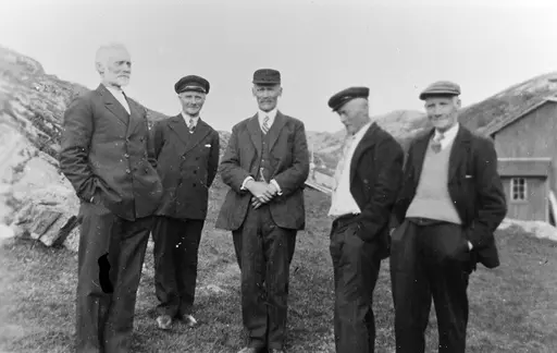 Fem menn står ute ved en haug. Et hus kan sees i bakgrunnen til høyre.