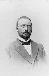 Portrett av en mann med bart og briller.