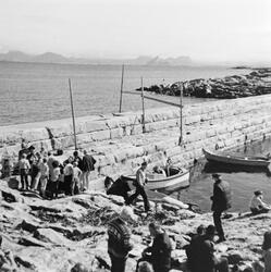 Mange mennesker ved moloen i Valvær, to båter, berg, hav og 