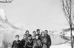 Ni barn fotografert ved et vann/hav. Hav, busker, fjell, snø