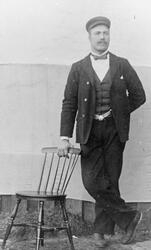 Portrett av en mann som står ved siden av en stol og holder 