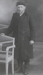 Portrett av en eldre mann, han står ved siden av en benk.