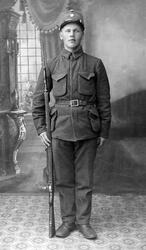 Portrett av soldat med gevær ved siden av seg. Bak til venst