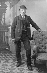 Portrett av en mann i stasklær og et smykke. Han står ved en