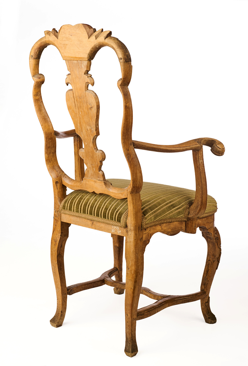 Stol av ask som hviler på fire ben. Gjennombrutt rygg bestående av C-former, samt symmetrisk svunget ryggbrett. På øvre og nedre del av ryggen symmetriske bladmotiv og skjell. Trapesformet sete, trukket med sekundært grønnfarget tekstil. Svungne armlener. Sargen er buet, innsvinget på midten og med utskåret skjellmotiv. Cabrioleformede forben med utskåret skjellornamentikk og klo og kule, samt svungne bakben. H-kryss mellom benene.