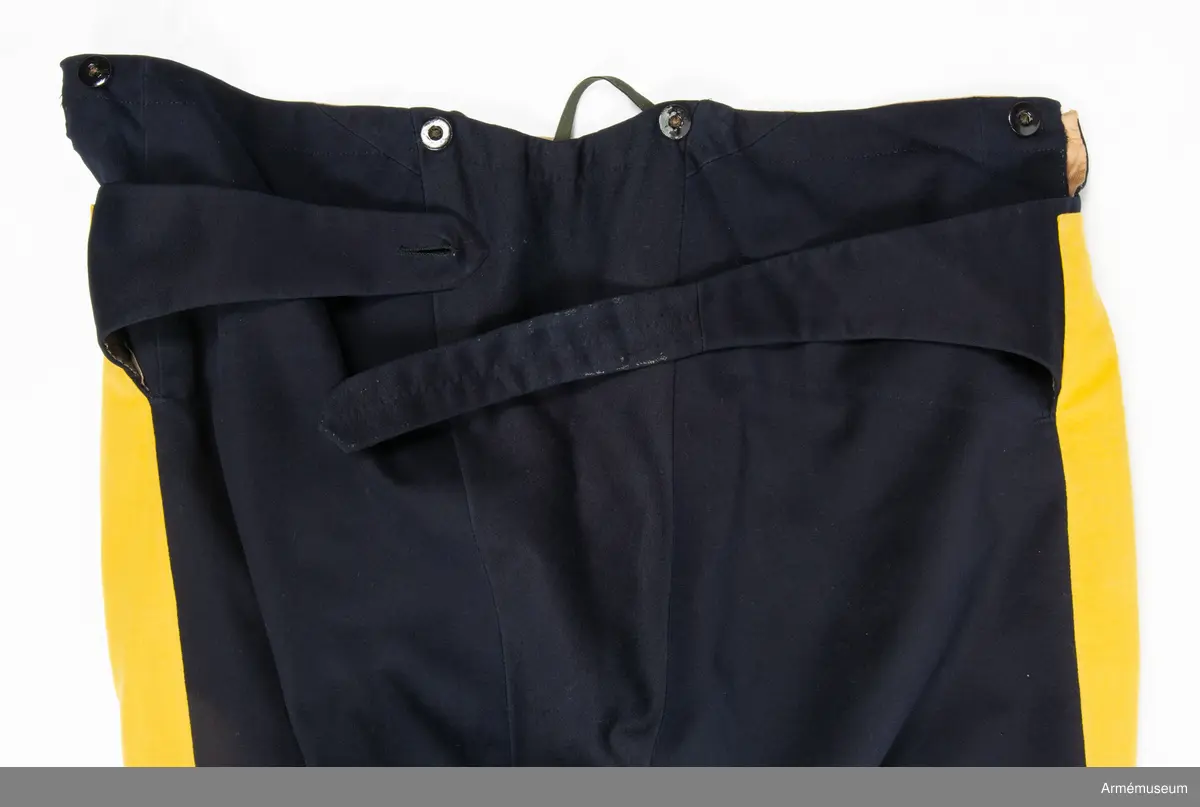 Mörkblå långbyxor med dubbla gula revärer i sidorna.

Byxorna är sydda av fint mörkblått kläde och är konstruerade med två fram- och två bakstycken, ett litet ok bak och hel lucka fram som knäpps i varje sida med en knapp. I varje sida av luckan sitter vidare en spänntamp fodrad med brunt linne- eller hampatyg som är avsedd att spännas ihop baktill för att reglera midjevidden.
Byxorna är ofodrade men har infodring i midjan och i luckan av oblekt linne- eller hampatyg, och ovanpå detta ytterligare en (troligen sekundär) infodring av oblekt bomullstyg. De har sytts om vid minst ett tillfälle då en mycket bred kil har satts in i grensömmen bak för att öka vidden.
Inuti byxorna sitter en förstärkning av oblekt bomullstyg i grenen. I byxbenens sidor sitter ca 5 cm breda dubbla revärer av fint gult kläde med en smal passpoal av gult kläde mellan. Nertill i fållen av varje ben sitter fastsydda ca 7-8 cm breda hälremmar av brunt skinn, samt på benens insida framtill en förstärkning av oblekt linne- eller hampatyg. Byxorna har fyra knappar fram i linningen och två bak för fastsättning av hängslen. Samtliga knappar är av svartlackad metall.
Byxorna har påskrift med svart bläck på luckans insida:
"46,371. Tillh. Genereallöjt. M. Thulstrup. G. af. enkefru H. C. Thulstrup".