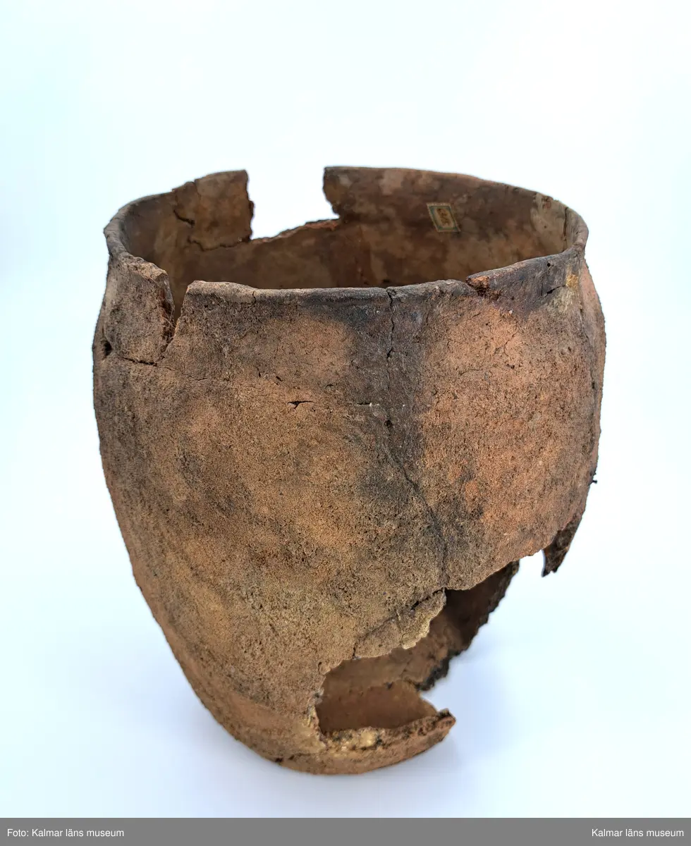 KLM 6315. Gravurna, nästan komplett urna. Höjd 28 cm, Mynningsdiameter 19 cm, Godstjocklek ca 8 mm. Tunnformad fint rabbad kruka med aningen övervikt mynning. Magrad med krossad granit. Oxiderat bränd (syrerik miljö). Grovt lerkärl utan öra.