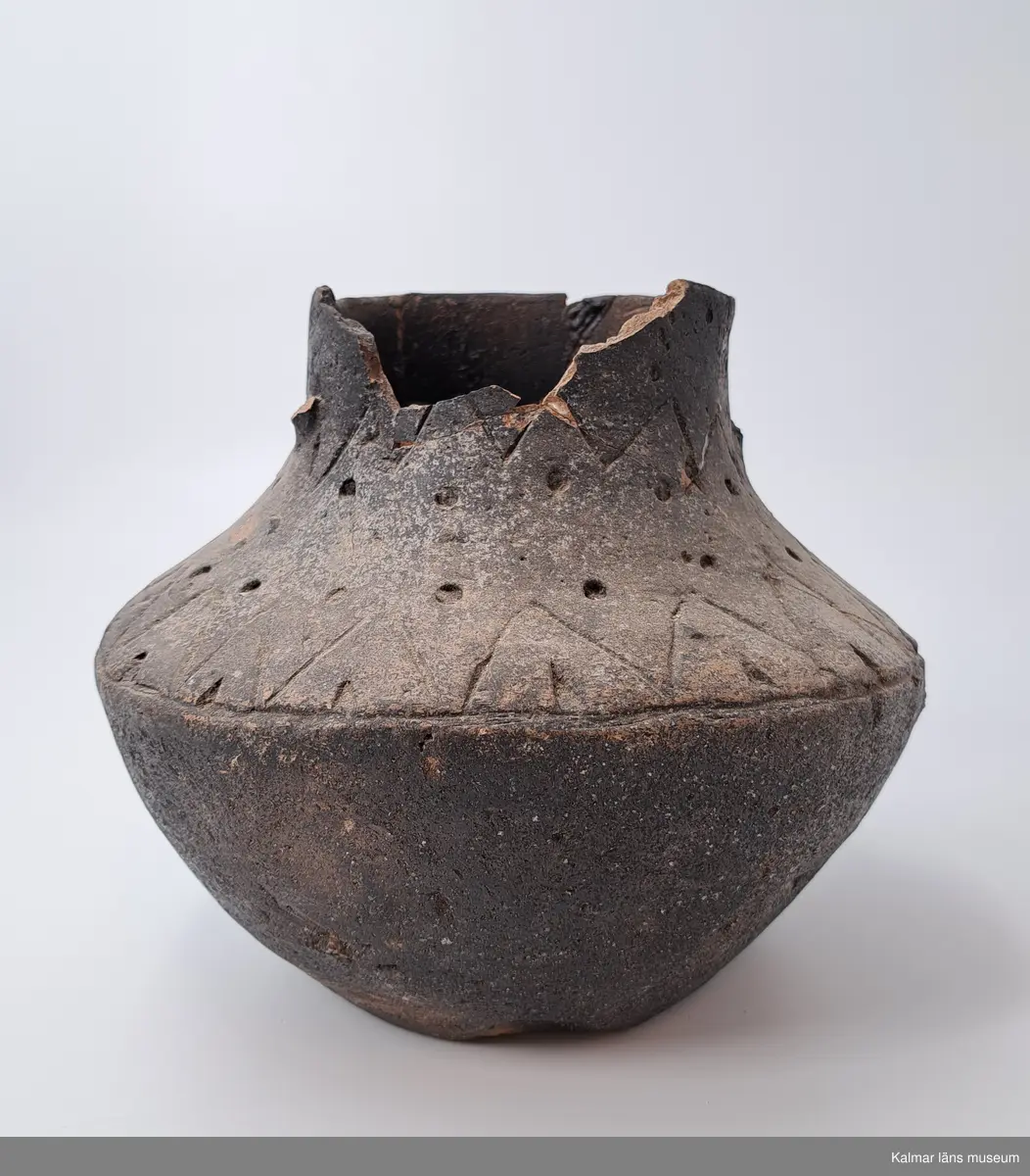 KLM 226. Gravurna. Av lera. Kärl med fast tunt gods, väl slammat och med svartgrå yta. Kärlet har haft två motsatta bygelformade öron. Dubbelkonisk kärlform. Kärlets nedre del utböjd, men den övre delen tvärt inböjd med rakt uppstående cylinderformig överdel, varigenom bukigheten blir skarpkantig.