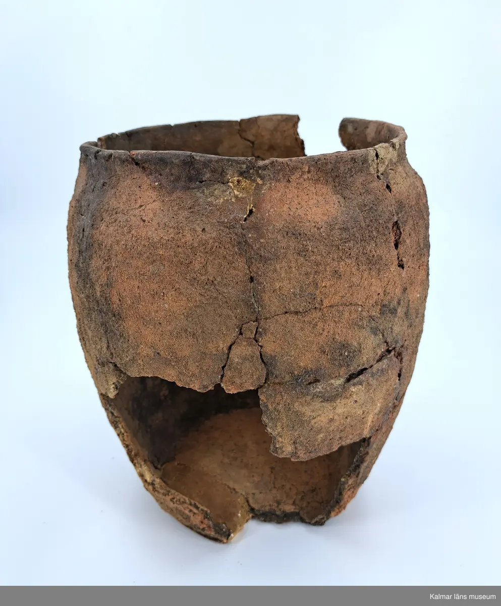 KLM 6315. Gravurna, nästan komplett urna. Höjd 28 cm, Mynningsdiameter 19 cm, Godstjocklek ca 8 mm. Tunnformad fint rabbad kruka med aningen övervikt mynning. Magrad med krossad granit. Oxiderat bränd (syrerik miljö). Grovt lerkärl utan öra.