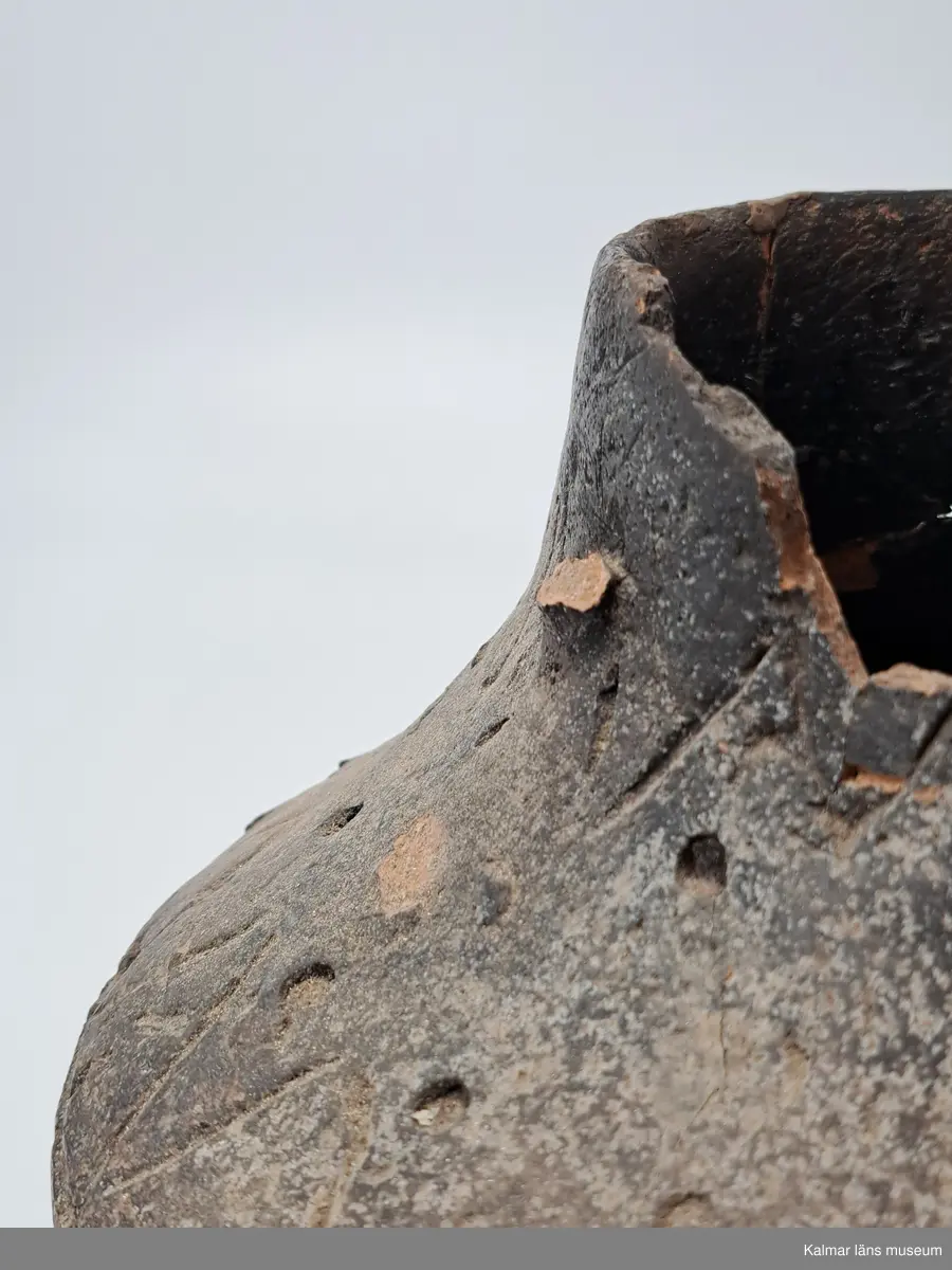 KLM 226. Gravurna. Av lera. Kärl med fast tunt gods, väl slammat och med svartgrå yta. Kärlet har haft två motsatta bygelformade öron. Dubbelkonisk kärlform. Kärlets nedre del utböjd, men den övre delen tvärt inböjd med rakt uppstående cylinderformig överdel, varigenom bukigheten blir skarpkantig.