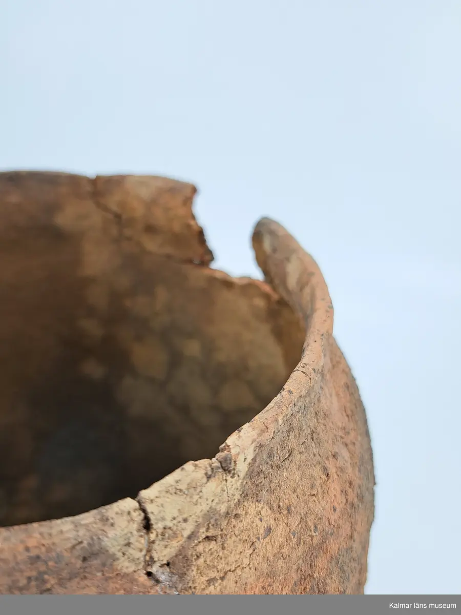 KLM 6315. Gravurna, nästan komplett urna. Höjd 28 cm, Mynningsdiameter 19 cm, Godstjocklek ca 8 mm. Tunnformad fint rabbad kruka med aningen övervikt mynning. Magrad med krossad granit. Oxiderat bränd (syrerik miljö). Grovt lerkärl utan öra.