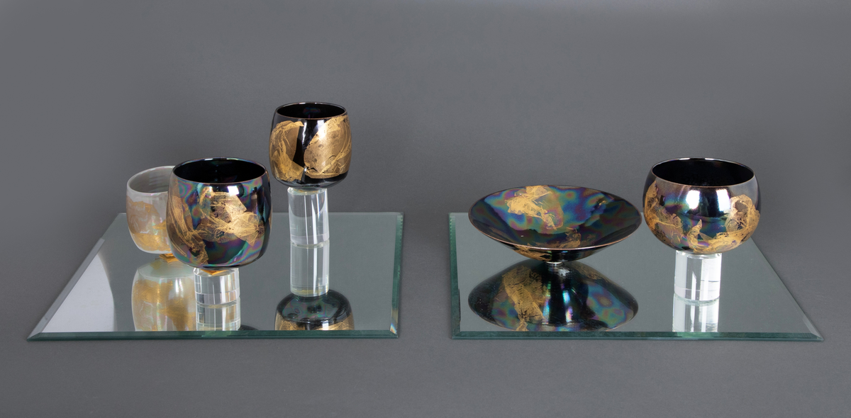 En skål og fire boller i porselen, montert på to kvadratiske speil. På det ene speilet står skålen samt en av bollene på en sylinderformet sokkel i klart glass. På det andre speilet står tre boller, to av dem på sylinderformede sokler i klart glass.