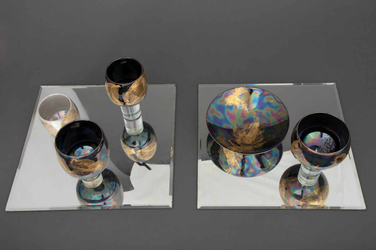 En skål og fire boller i porselen, montert på to kvadratiske speil. På det ene speilet står skålen samt en av bollene på en sylinderformet sokkel i klart glass. På det andre speilet står tre boller, to av dem på sylinderformede sokler i klart glass.