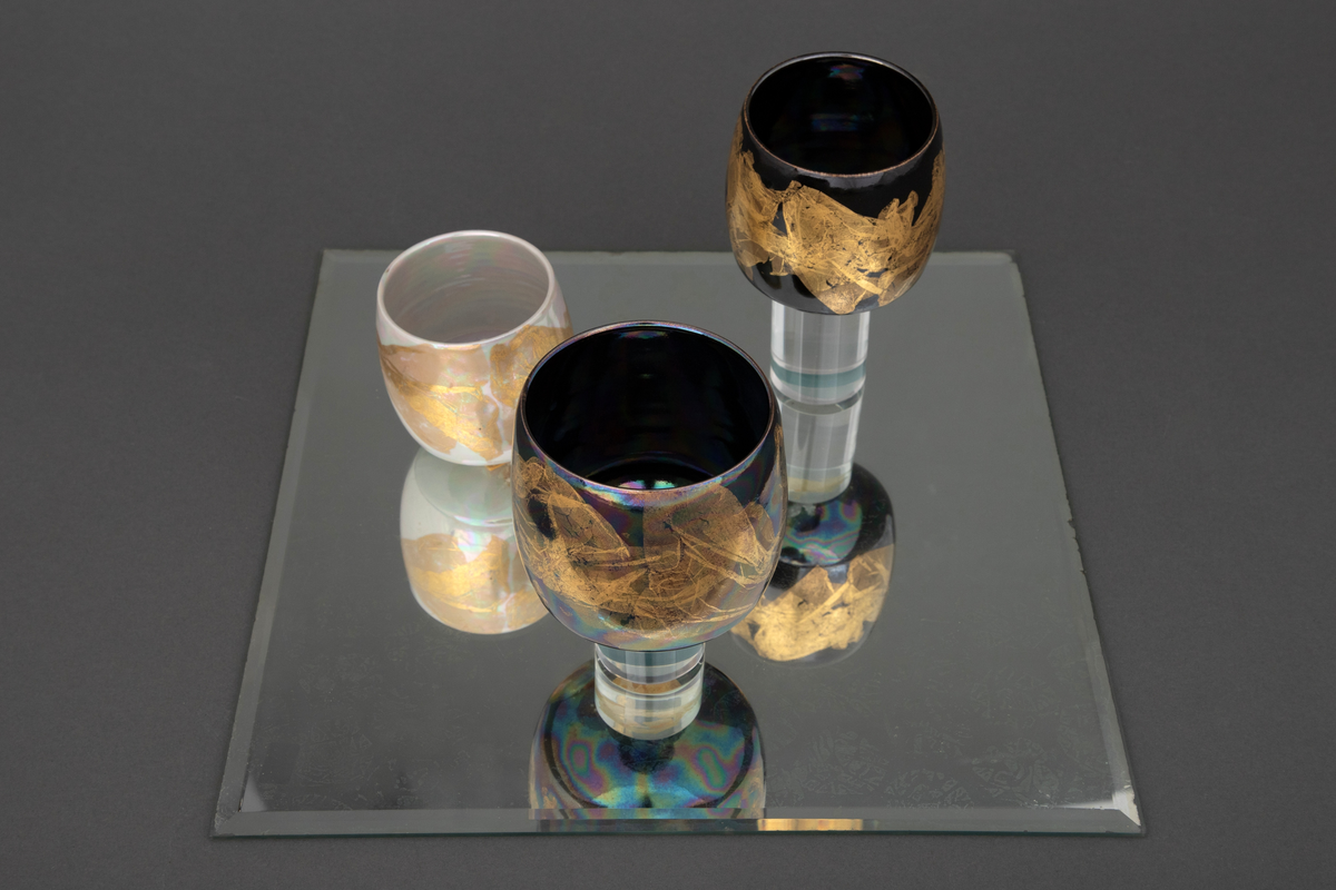 En skål og fire boller i porselen, montert på to kvadratiske speil. På det ene speilet står skålen samt en av bollene på en sylinderformet sokkel i klart glass. På det andre speilet står tre boller, to av dem på sylinderformede sokler i klart glass.