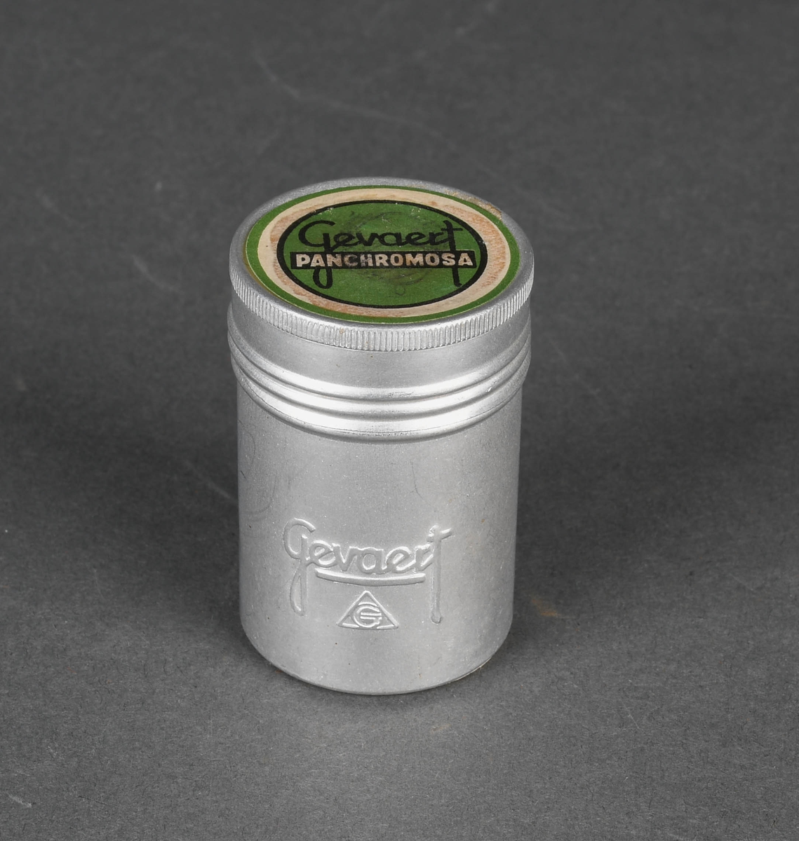 Sylindrisk beholder i metall. Todelt med stort hovedrom og mindre lokk. Lukkemekanisme består av gjenger.