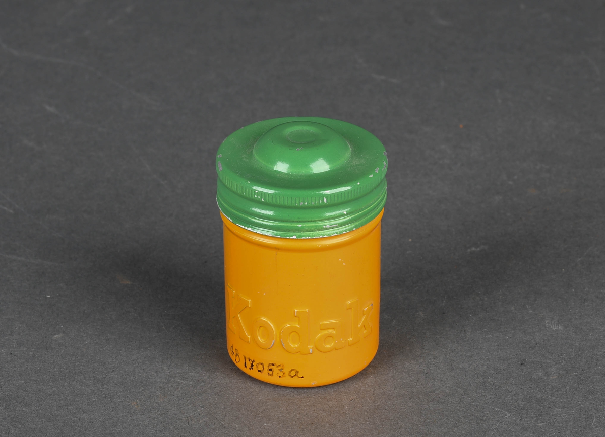 Sylindrisk boks i aluminium, malt gul og grønn. Gjenger for å feste beholder og lokk.