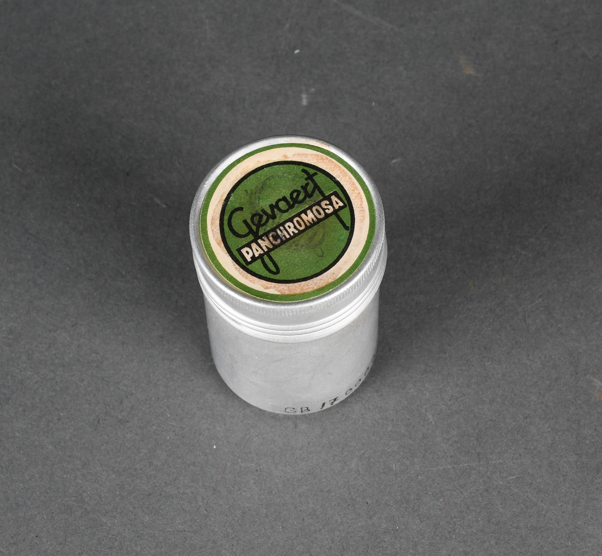 Sylindrisk beholder i metall. Todelt med stort hovedrom og mindre lokk. Lukkemekanisme består av gjenger.