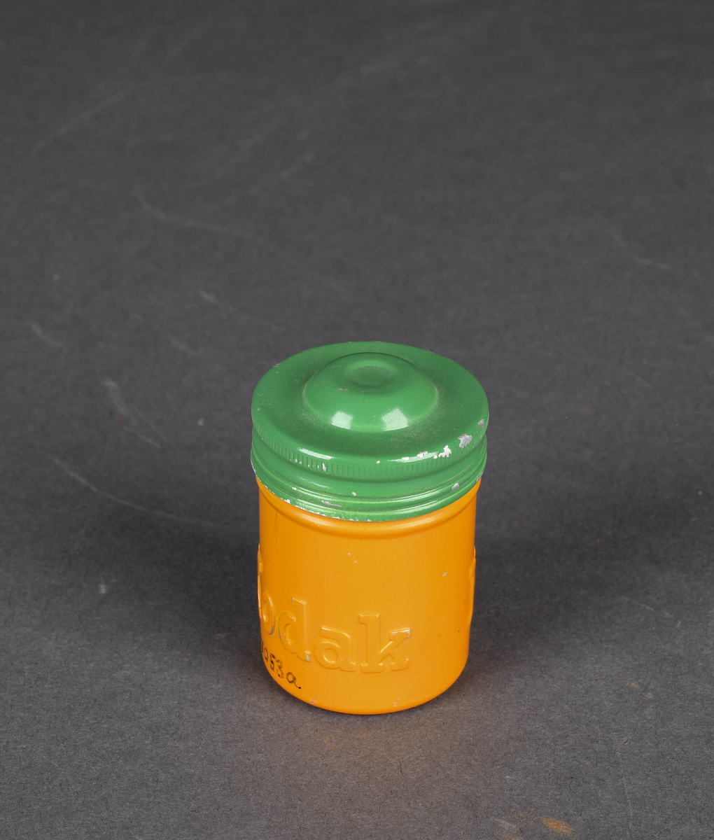 Sylindrisk boks i aluminium, malt gul og grønn. Gjenger for å feste beholder og lokk.