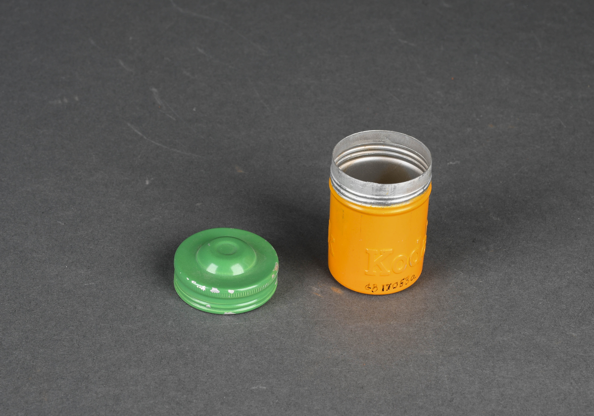 Sylindrisk boks i aluminium, malt gul og grønn. Gjenger for å feste beholder og lokk.