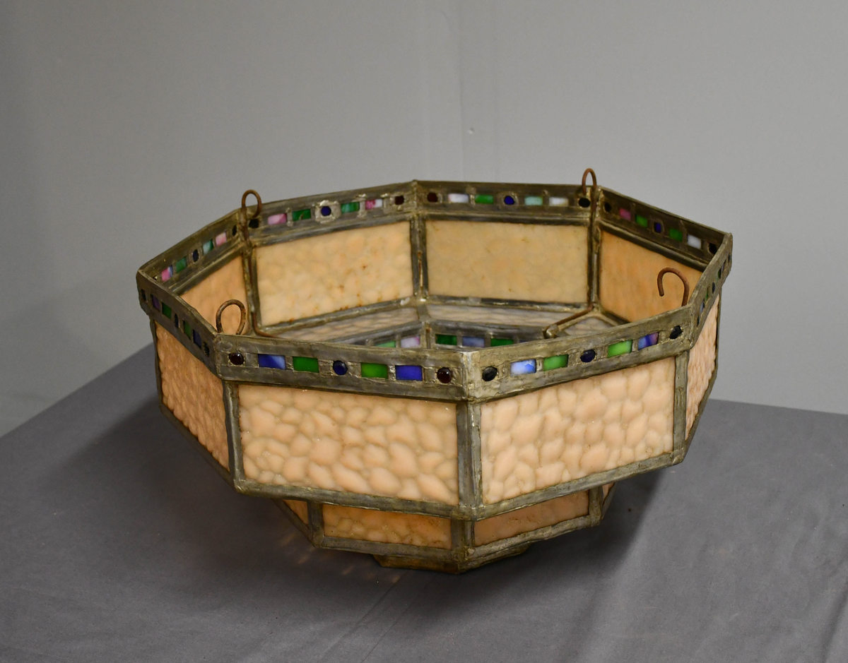 Åttekantet lampeskjerm av blyglass. Farget glass. Bygd opp i tre etasjer, smalner nedover. Fire blykroker loddet fast øverst. Åttetagget stjerne nedderst.