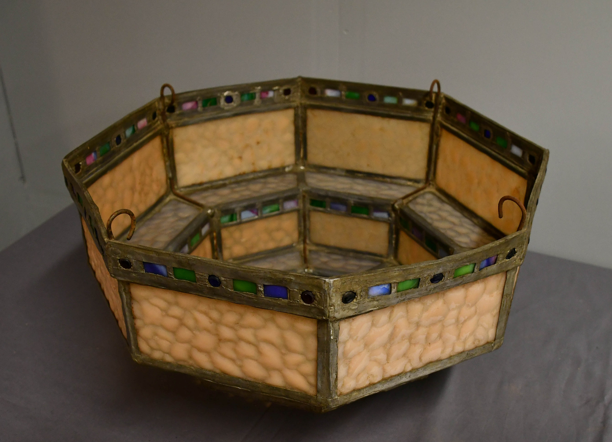 Åttekantet lampeskjerm av blyglass. Farget glass. Bygd opp i tre etasjer, smalner nedover. Fire blykroker loddet fast øverst. Åttetagget stjerne nedderst.