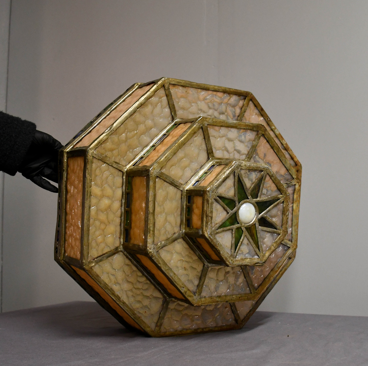 Åttekantet lampeskjerm av blyglass. Farget glass. Bygd opp i tre etasjer, smalner nedover. Fire blykroker loddet fast øverst. Åttetagget stjerne nedderst.