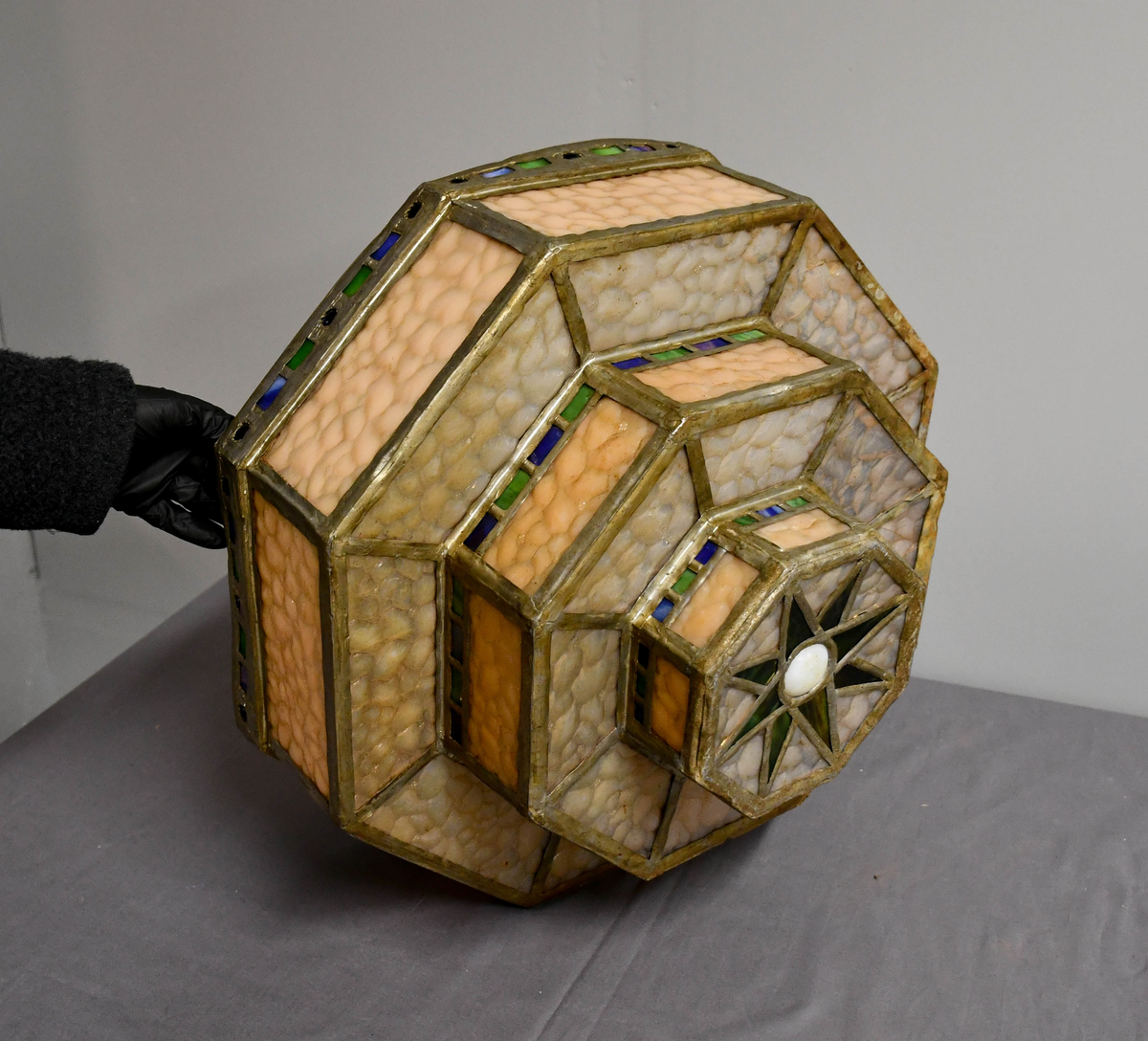 Åttekantet lampeskjerm av blyglass. Farget glass. Bygd opp i tre etasjer, smalner nedover. Fire blykroker loddet fast øverst. Åttetagget stjerne nedderst.