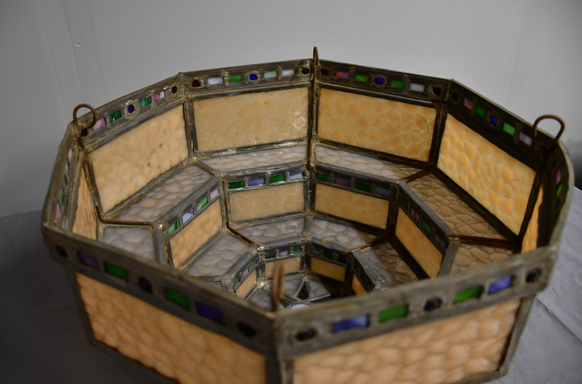 Åttekantet lampeskjerm av blyglass. Farget glass. Bygd opp i tre etasjer, smalner nedover. Fire blykroker loddet fast øverst. Åttetagget stjerne nedderst.