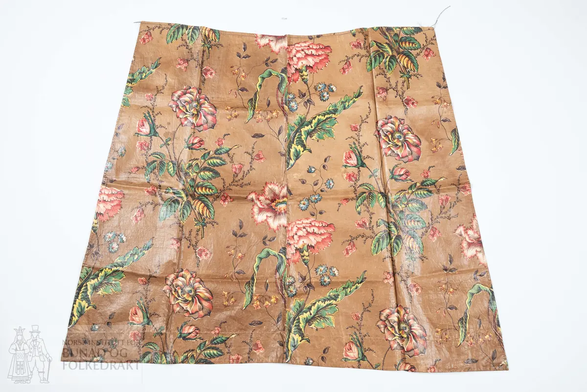 Forkle.
Forkledet er omsydd.
Trykt, glansfullt chintz. Saum midt foran, attersting og overkasting med lyst silkegarn.
Skonert langs nedkanten med eit 5 cm breitt, trykt bomullstøy.
Dette er falda til langs skoneringas øvre kant. Nederst er det bretta dobbel, smal fald på forkletøyet, som er falda til i skoneringa.
Sidene er truleg sekundære då dei er skråklypte. Dei har dobbel smal fald, sauma til med små faldesting, men trådtypa er annleis og yngre.
I livet er det bretta ned ca 1 cm som er stikka ned med ein maskinsaum.