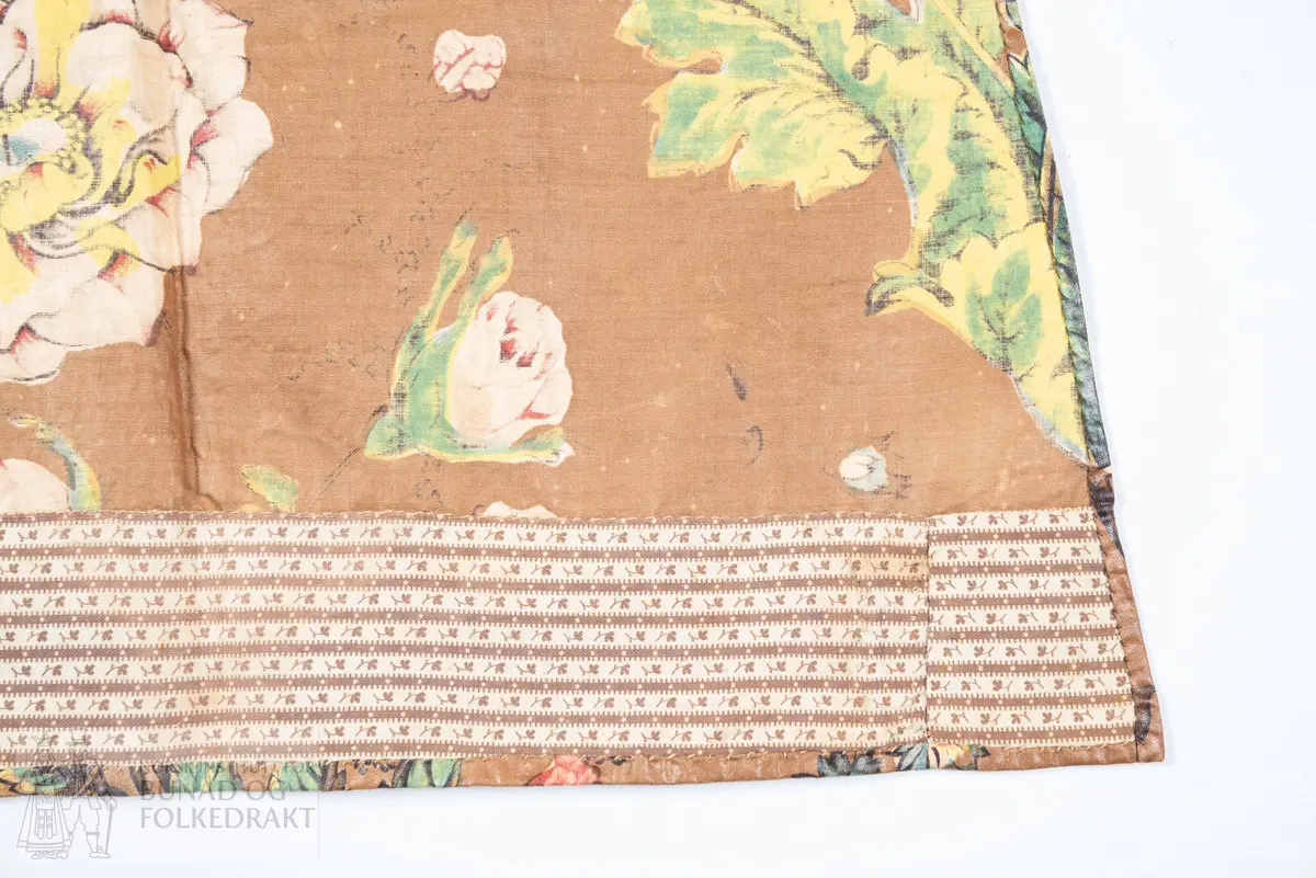 Forkle.
Forkledet er omsydd.
Trykt, glansfullt chintz. Saum midt foran, attersting og overkasting med lyst silkegarn.
Skonert langs nedkanten med eit 5 cm breitt, trykt bomullstøy.
Dette er falda til langs skoneringas øvre kant. Nederst er det bretta dobbel, smal fald på forkletøyet, som er falda til i skoneringa.
Sidene er truleg sekundære då dei er skråklypte. Dei har dobbel smal fald, sauma til med små faldesting, men trådtypa er annleis og yngre.
I livet er det bretta ned ca 1 cm som er stikka ned med ein maskinsaum.