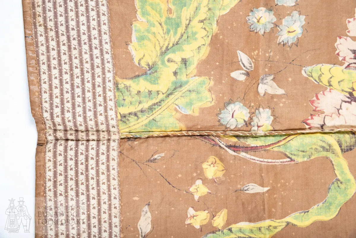 Forkle.
Forkledet er omsydd.
Trykt, glansfullt chintz. Saum midt foran, attersting og overkasting med lyst silkegarn.
Skonert langs nedkanten med eit 5 cm breitt, trykt bomullstøy.
Dette er falda til langs skoneringas øvre kant. Nederst er det bretta dobbel, smal fald på forkletøyet, som er falda til i skoneringa.
Sidene er truleg sekundære då dei er skråklypte. Dei har dobbel smal fald, sauma til med små faldesting, men trådtypa er annleis og yngre.
I livet er det bretta ned ca 1 cm som er stikka ned med ein maskinsaum.