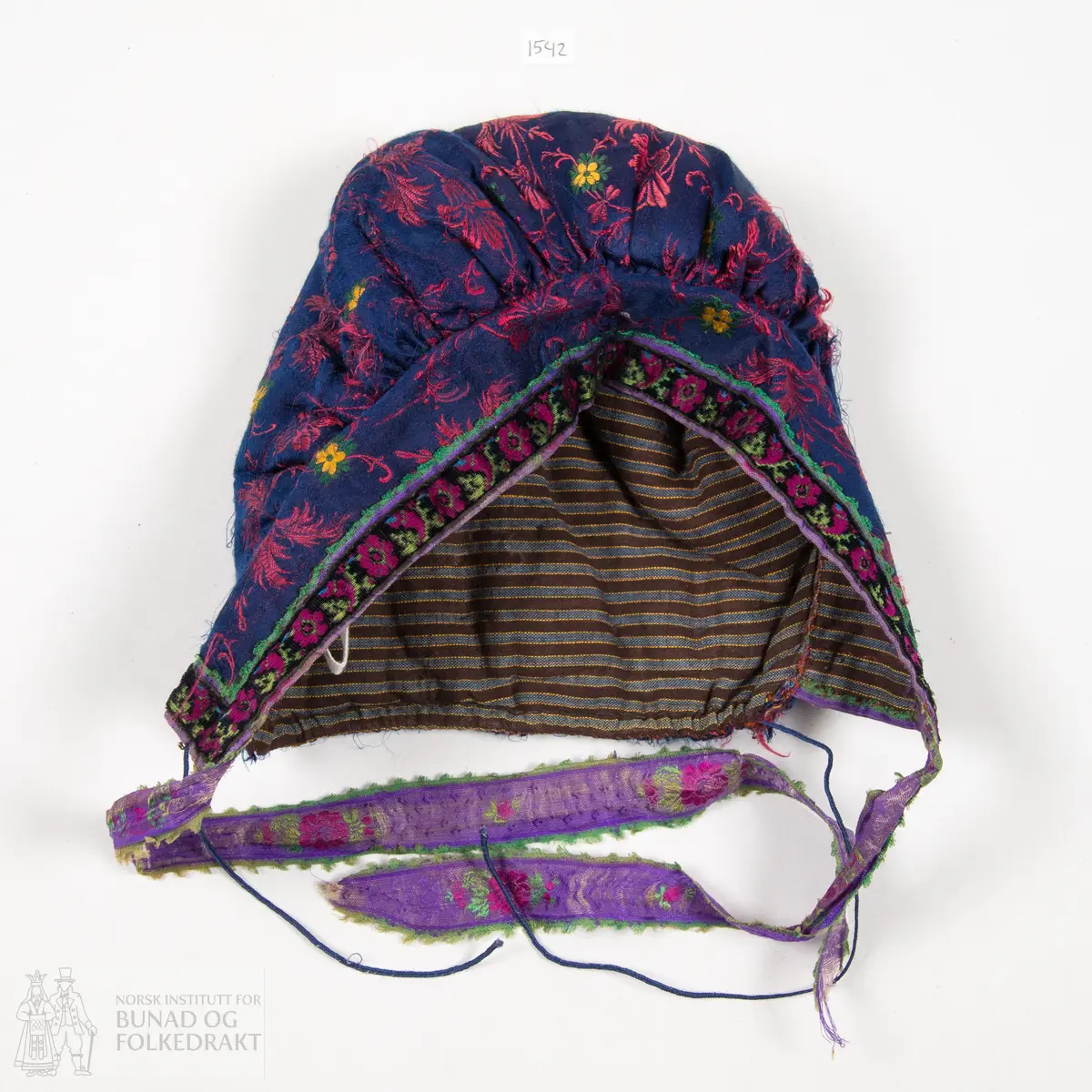 Rynkelue, kvadratisk pull rynka til eit rektangulært pannestykkje. Hovudstoff av satengvove blomemønstra silkestoff. Fòr av stripevove bomullslerret. Pullstykkjet er kraftig vattert med mjuk tjukk vatt, medan pannestykkjet er utan mellomfor. Løpegang med trekksnor i nedkant av pullstykkjet. Knyteband av bomull/silke, med vove blomemønster. Dette bandet er også brukt til kanting av pannestykkjet. Oppå dette er sydd blomemønstra fløyelsband. Heile lua er handsydd.