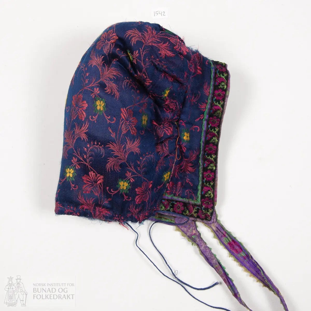 Rynkelue, kvadratisk pull rynka til eit rektangulært pannestykkje. Hovudstoff av satengvove blomemønstra silkestoff. Fòr av stripevove bomullslerret. Pullstykkjet er kraftig vattert med mjuk tjukk vatt, medan pannestykkjet er utan mellomfor. Løpegang med trekksnor i nedkant av pullstykkjet. Knyteband av bomull/silke, med vove blomemønster. Dette bandet er også brukt til kanting av pannestykkjet. Oppå dette er sydd blomemønstra fløyelsband. Heile lua er handsydd.