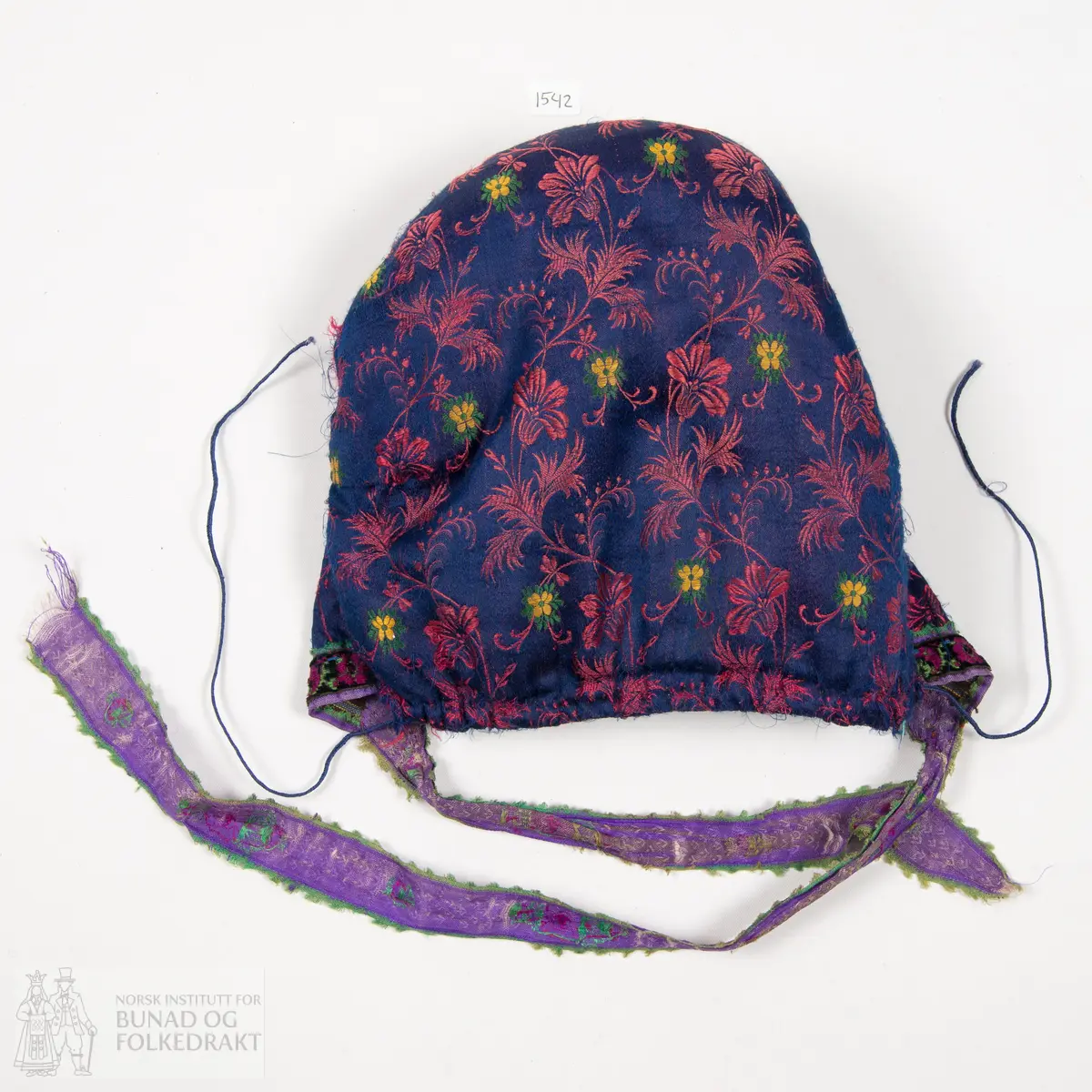 Rynkelue, kvadratisk pull rynka til eit rektangulært pannestykkje. Hovudstoff av satengvove blomemønstra silkestoff. Fòr av stripevove bomullslerret. Pullstykkjet er kraftig vattert med mjuk tjukk vatt, medan pannestykkjet er utan mellomfor. Løpegang med trekksnor i nedkant av pullstykkjet. Knyteband av bomull/silke, med vove blomemønster. Dette bandet er også brukt til kanting av pannestykkjet. Oppå dette er sydd blomemønstra fløyelsband. Heile lua er handsydd.