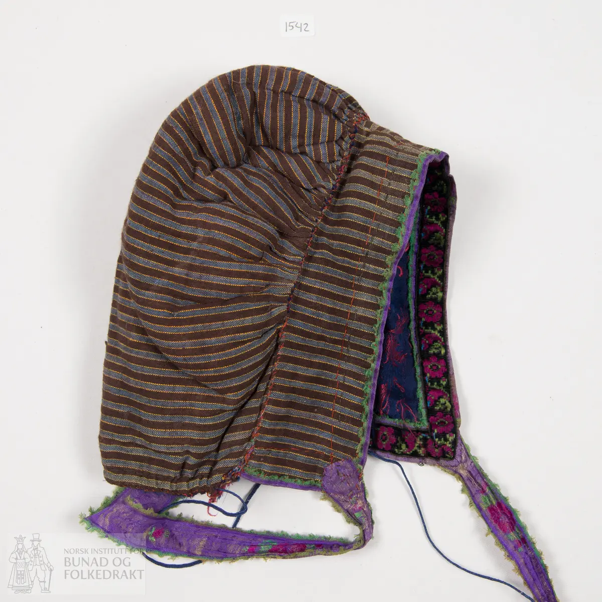 Rynkelue, kvadratisk pull rynka til eit rektangulært pannestykkje. Hovudstoff av satengvove blomemønstra silkestoff. Fòr av stripevove bomullslerret. Pullstykkjet er kraftig vattert med mjuk tjukk vatt, medan pannestykkjet er utan mellomfor. Løpegang med trekksnor i nedkant av pullstykkjet. Knyteband av bomull/silke, med vove blomemønster. Dette bandet er også brukt til kanting av pannestykkjet. Oppå dette er sydd blomemønstra fløyelsband. Heile lua er handsydd.