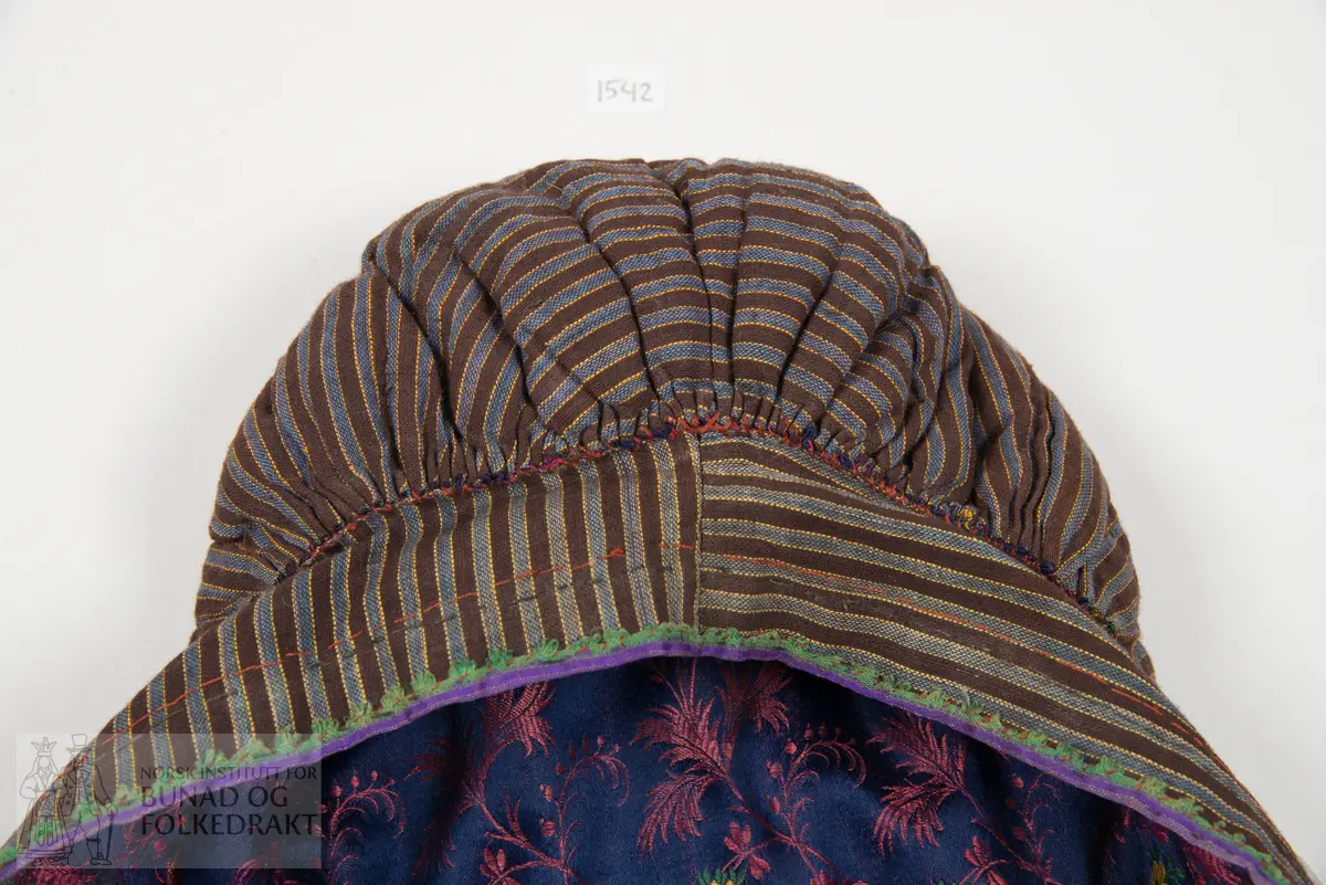 Rynkelue, kvadratisk pull rynka til eit rektangulært pannestykkje. Hovudstoff av satengvove blomemønstra silkestoff. Fòr av stripevove bomullslerret. Pullstykkjet er kraftig vattert med mjuk tjukk vatt, medan pannestykkjet er utan mellomfor. Løpegang med trekksnor i nedkant av pullstykkjet. Knyteband av bomull/silke, med vove blomemønster. Dette bandet er også brukt til kanting av pannestykkjet. Oppå dette er sydd blomemønstra fløyelsband. Heile lua er handsydd.