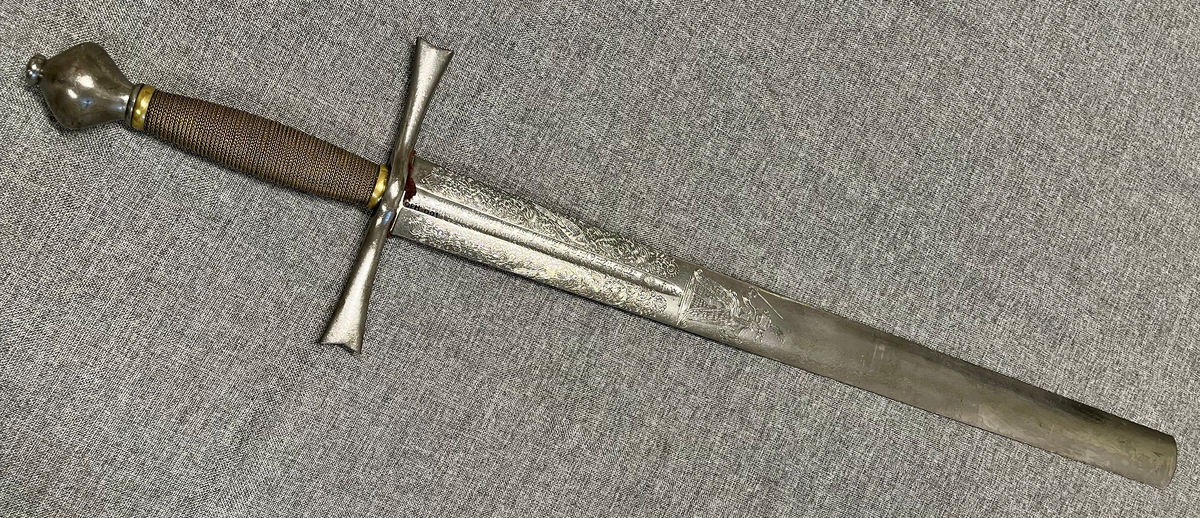 Langt tveegget sverd i stål med rett, butt klinge med kort blodrand på hver side. Klingen er rikt utsmykket med etsinger eller inngraveringer og flere merker som kan være smedmerker, blant annet en sol med menneskeansikt. Dekorert med blomsterranker, fugle- og dyremotiver og gudinnen Justitia. Grepet har hjerteformet knapp avsluttet med en mindre knapp. Stålgrep viklet med tvunnet messingtråd og satt med messingbånd oppe og nede. Symetrisk feste med flate pilformede parerstenger som smalner inn mot midten.