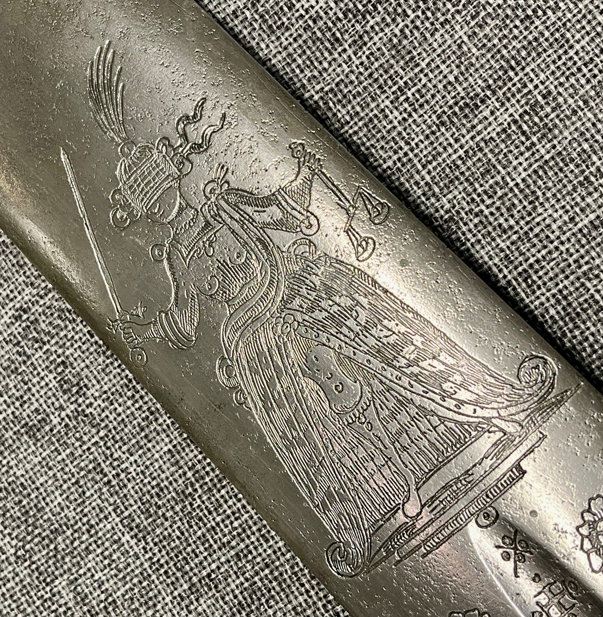 Langt tveegget sverd i stål med rett, butt klinge med kort blodrand på hver side. Klingen er rikt utsmykket med etsinger eller inngraveringer og flere merker som kan være smedmerker, blant annet en sol med menneskeansikt. Dekorert med blomsterranker, fugle- og dyremotiver og gudinnen Justitia. Grepet har hjerteformet knapp avsluttet med en mindre knapp. Stålgrep viklet med tvunnet messingtråd og satt med messingbånd oppe og nede. Symetrisk feste med flate pilformede parerstenger som smalner inn mot midten.