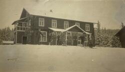 Skiløpere, foran en stort bygning i sveitserstil. Muligens e