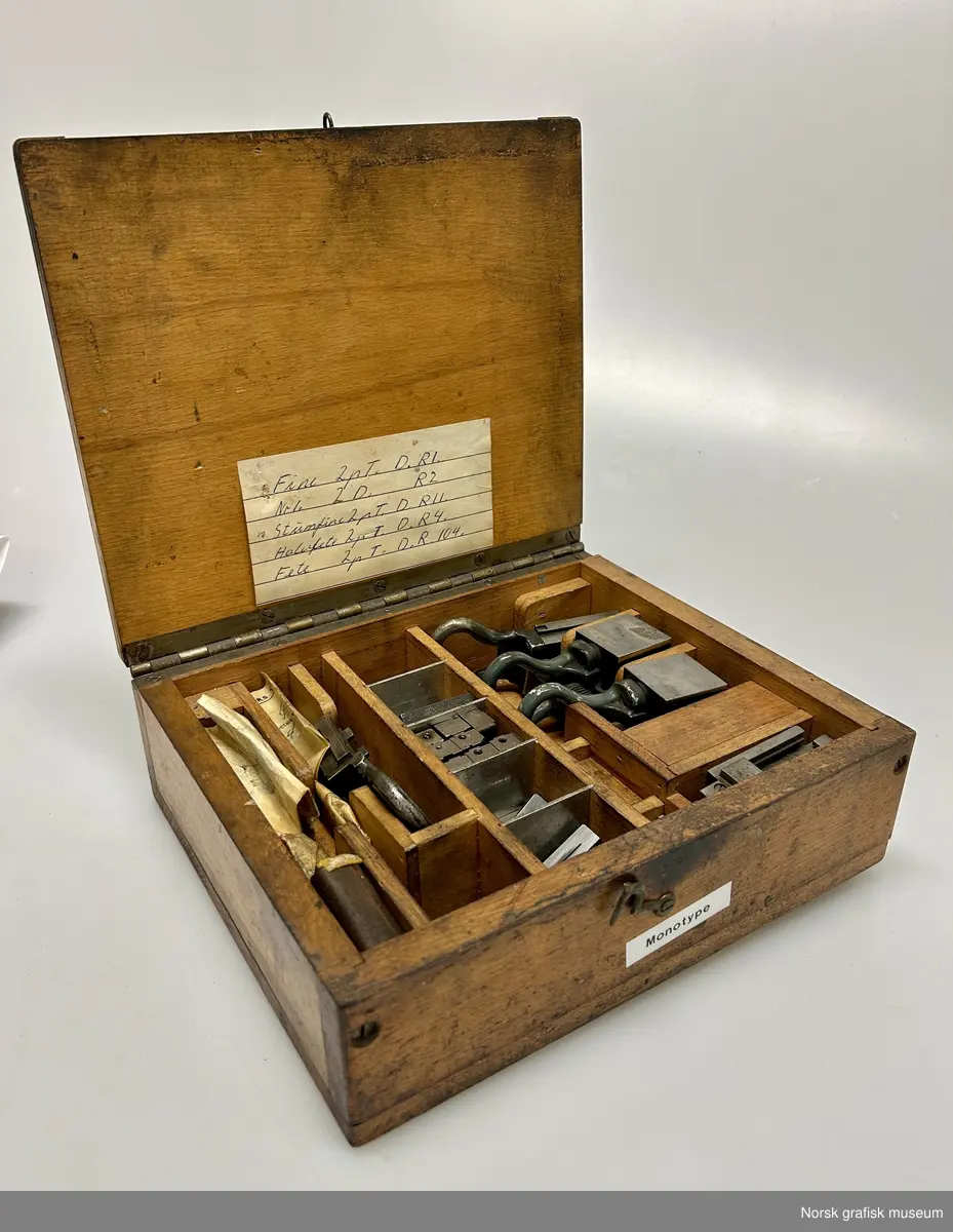 Et trestrin inneholdende flere mindre ulike deler i metall. Skrinet er merket med "Monotype", så delen er trolig til en slik maskin.