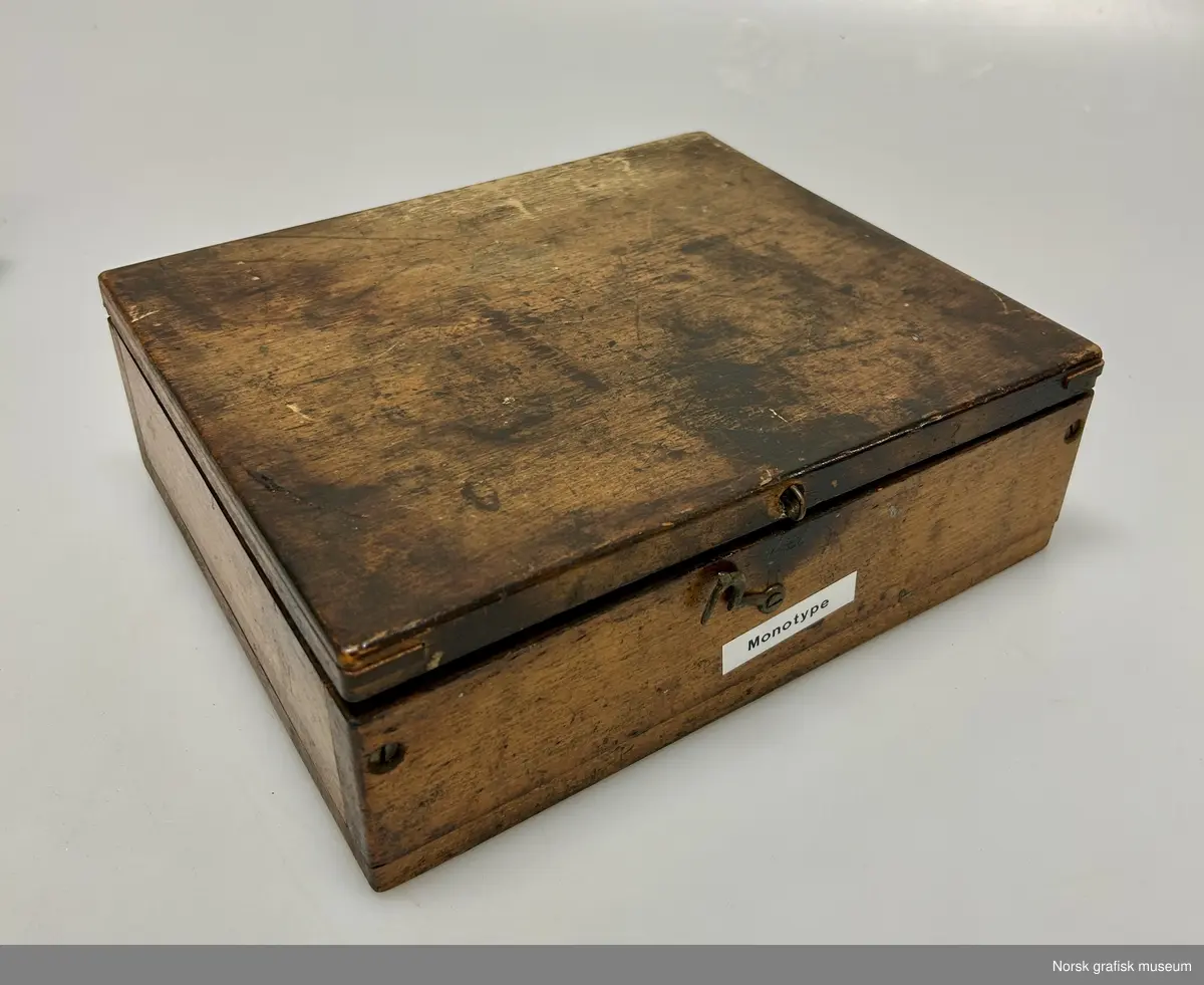 Et trestrin inneholdende flere mindre ulike deler i metall. Skrinet er merket med "Monotype", så delen er trolig til en slik maskin.