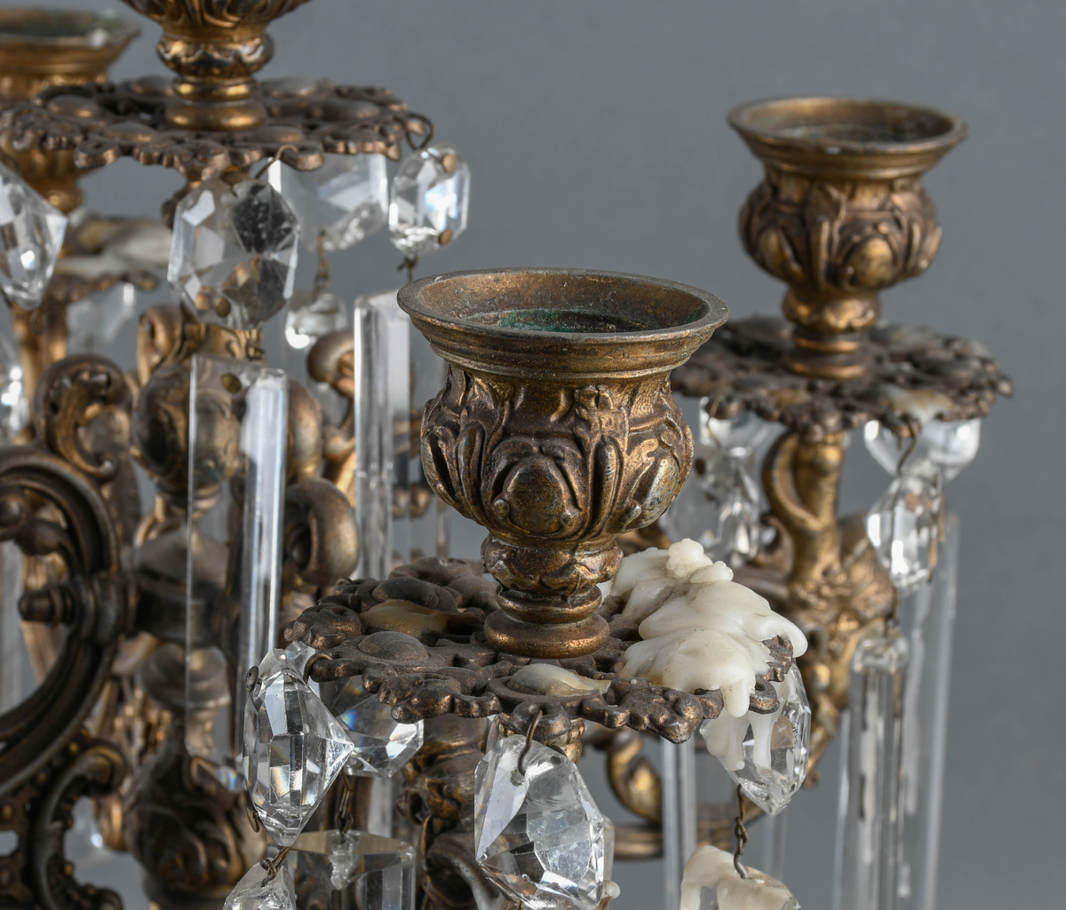 Kandelaber av messing med prismer hengende på. Fire lysholdere med prismer rundt mansjettene. I midten går selve staken opp i en lysholder med avtagbar propp. Foten er sterkt profilert i rikt mønstret støpegods. Det mangler noen prismer.