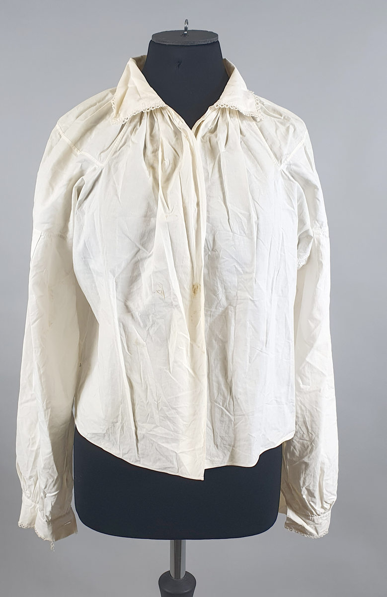 Hvit bunadsskjorte av bomull, med nupereller på mansjetter og krage. Åpning foran helt ned. På mansjettene er nuperellene løsnet enkelte steder