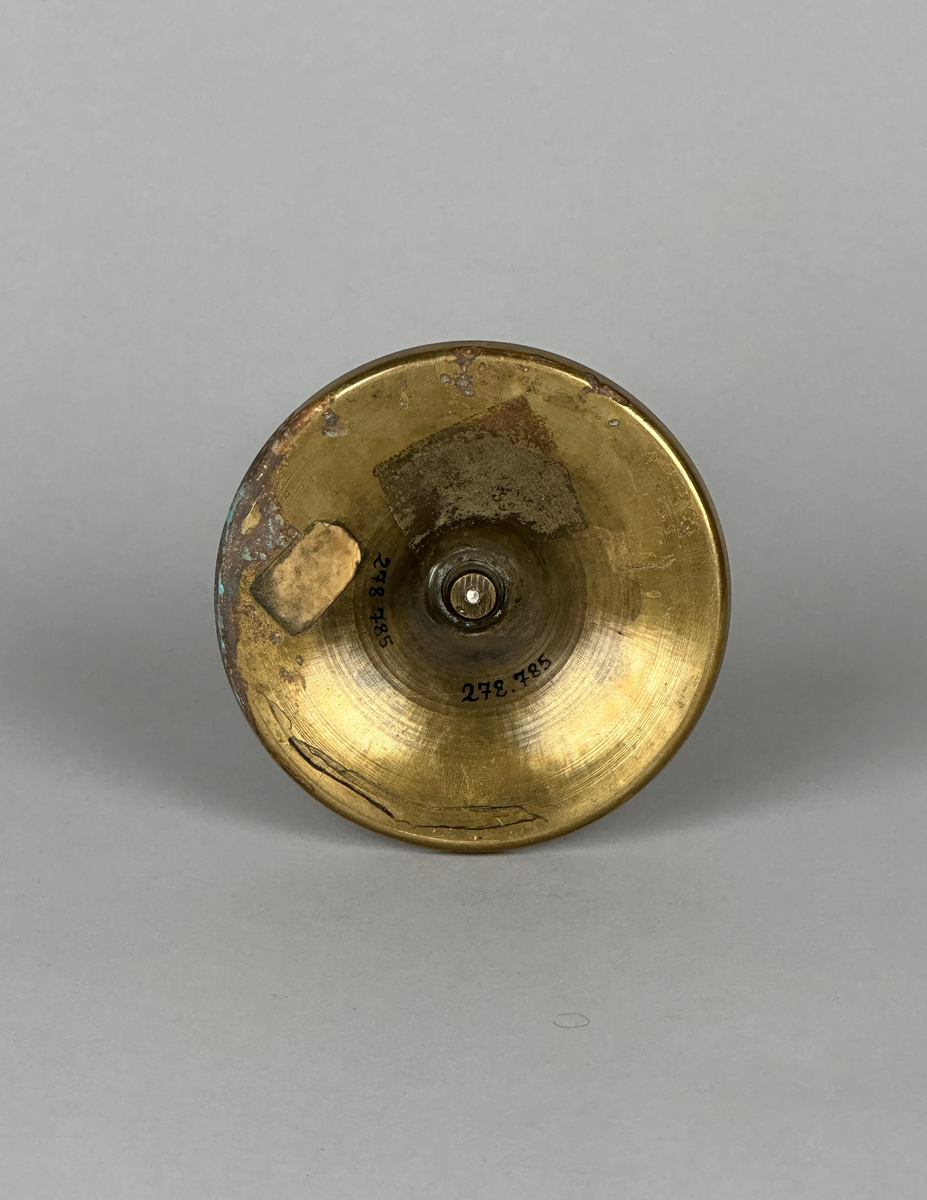 Ljusstake av mässing, i två delar. Lite skålformat brätte på ljuspipan. Svagt balusterformad stake med gängad fot. Fotens kant är tvärt uppvikt.