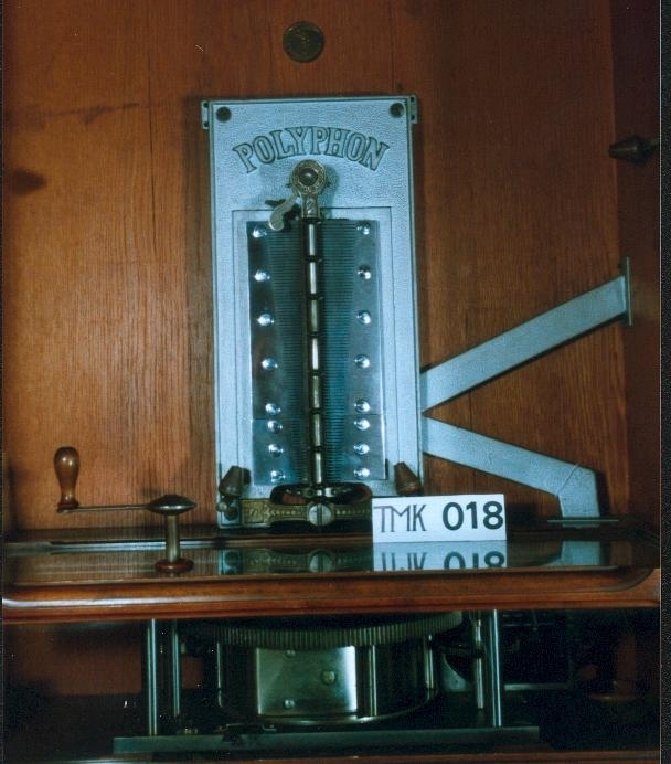 Vertikalstående, stor spilledåse av typen Polyphon, modell 54. Prod. nr. 3454. Maskinen bruker 63 cms plater.

Høyt skap i polert nøttetre med glassdør øverst og skuff nederst. Bak glassdøren ligger maskineriet og platearmen. Ved maskineriet ligger en lapp med bruksanvisning på tysk, engelsk og fransk. På skapetdøren, på hver side av glassplaten, står to rikt utskjærte dørsøyler. Øverst i hjørnene er det gjennombrudt akantus-utskjæringer. På høyre side av skapet er et myntinnkast som tar 5-øringer. Skuffen har to rikt utskjærte stolper og ornamentert metallhåndtak. Den åpnes på skrå og har plass til en rekke plater. Øverst i høyre hjørnet inne i skuffen er en mindre pengeskuff.

Til spilleren hører to små nøkler.