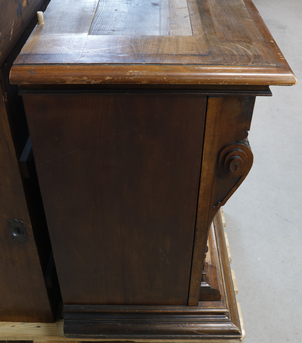 Vertikalstående, stor spilledåse av typen Polyphon, modell 54. Prod. nr. 3454. Maskinen bruker 63 cms plater.

Høyt skap i polert nøttetre med glassdør øverst og skuff nederst. Bak glassdøren ligger maskineriet og platearmen. Ved maskineriet ligger en lapp med bruksanvisning på tysk, engelsk og fransk. På skapetdøren, på hver side av glassplaten, står to rikt utskjærte dørsøyler. Øverst i hjørnene er det gjennombrudt akantus-utskjæringer. På høyre side av skapet er et myntinnkast som tar 5-øringer. Skuffen har to rikt utskjærte stolper og ornamentert metallhåndtak. Den åpnes på skrå og har plass til en rekke plater. Øverst i høyre hjørnet inne i skuffen er en mindre pengeskuff.

Til spilleren hører to små nøkler.