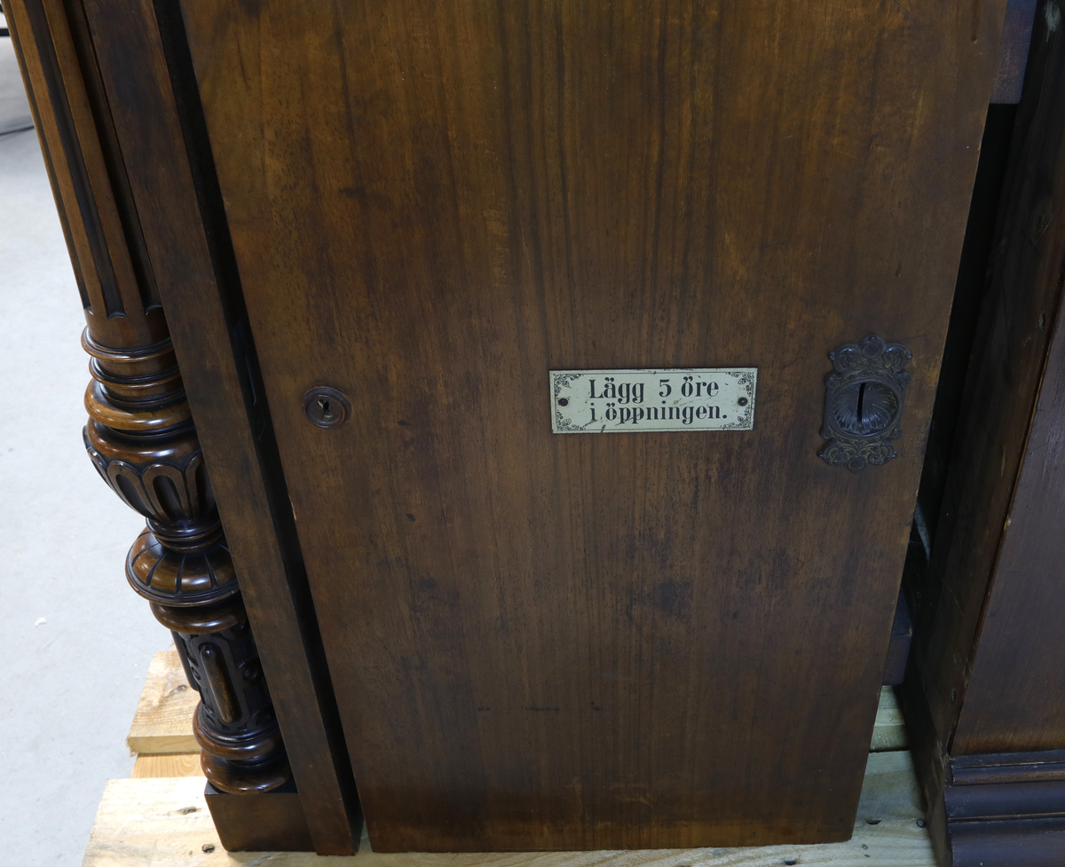 Vertikalstående, stor spilledåse av typen Polyphon, modell 54. Prod. nr. 3454. Maskinen bruker 63 cms plater.

Høyt skap i polert nøttetre med glassdør øverst og skuff nederst. Bak glassdøren ligger maskineriet og platearmen. Ved maskineriet ligger en lapp med bruksanvisning på tysk, engelsk og fransk. På skapetdøren, på hver side av glassplaten, står to rikt utskjærte dørsøyler. Øverst i hjørnene er det gjennombrudt akantus-utskjæringer. På høyre side av skapet er et myntinnkast som tar 5-øringer. Skuffen har to rikt utskjærte stolper og ornamentert metallhåndtak. Den åpnes på skrå og har plass til en rekke plater. Øverst i høyre hjørnet inne i skuffen er en mindre pengeskuff.

Til spilleren hører to små nøkler.