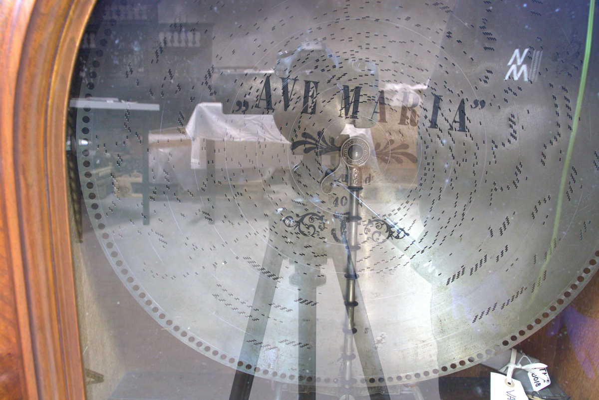 Vertikalstående, stor spilledåse av typen Polyphon, modell 54. Prod. nr. 3454. Maskinen bruker 63 cms plater.

Høyt skap i polert nøttetre med glassdør øverst og skuff nederst. Bak glassdøren ligger maskineriet og platearmen. Ved maskineriet ligger en lapp med bruksanvisning på tysk, engelsk og fransk. På skapetdøren, på hver side av glassplaten, står to rikt utskjærte dørsøyler. Øverst i hjørnene er det gjennombrudt akantus-utskjæringer. På høyre side av skapet er et myntinnkast som tar 5-øringer. Skuffen har to rikt utskjærte stolper og ornamentert metallhåndtak. Den åpnes på skrå og har plass til en rekke plater. Øverst i høyre hjørnet inne i skuffen er en mindre pengeskuff.

Til spilleren hører to små nøkler.